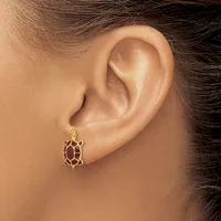 A gold turtle-shaped earring with a red enamel shell is worn on a pierced earlobe.