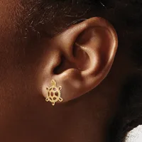 A gold ship wheel stud earring worn on the earlobe of a person with brown skin and dark hair.
