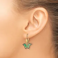 A person wearing a gold hook earring with a green and black enameled butterfly pendant hanging from their earlobe.