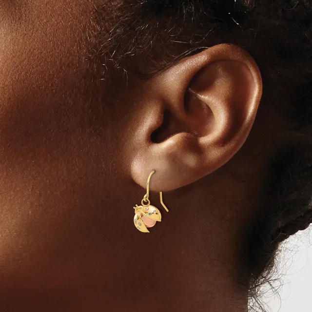 A close-up side view of a person wearing gold drop earrings with leaf-shaped pendants on wire hooks.