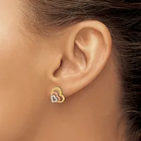 A person wearing a pair of interlocking heart stud earrings in gold and silver tones on their earlobe.