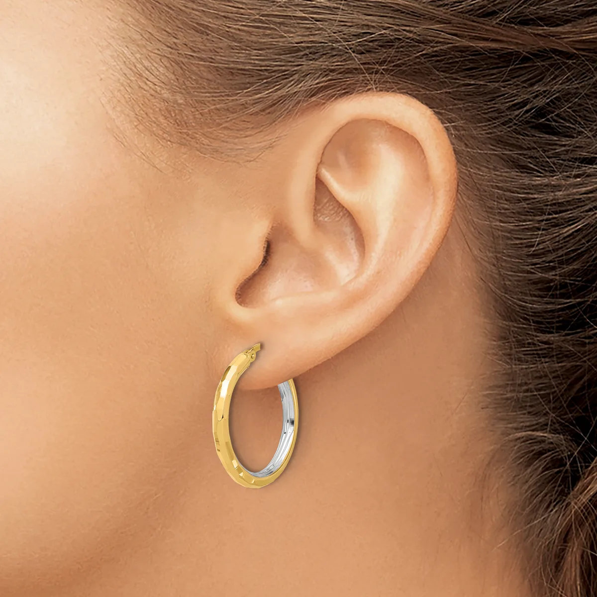 A person wearing two-tone hoop earrings with a textured gold finish and polished silver finish, shown from the side view against their ear.