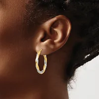 A person wearing two-tone twisted hoop earrings with a gold and silver finish, shown from the side profile of their head and neck.