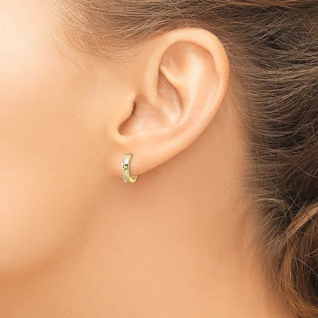 A person wearing a small gold hoop earring with a decorative pattern, shown from the side view of their ear and neck.