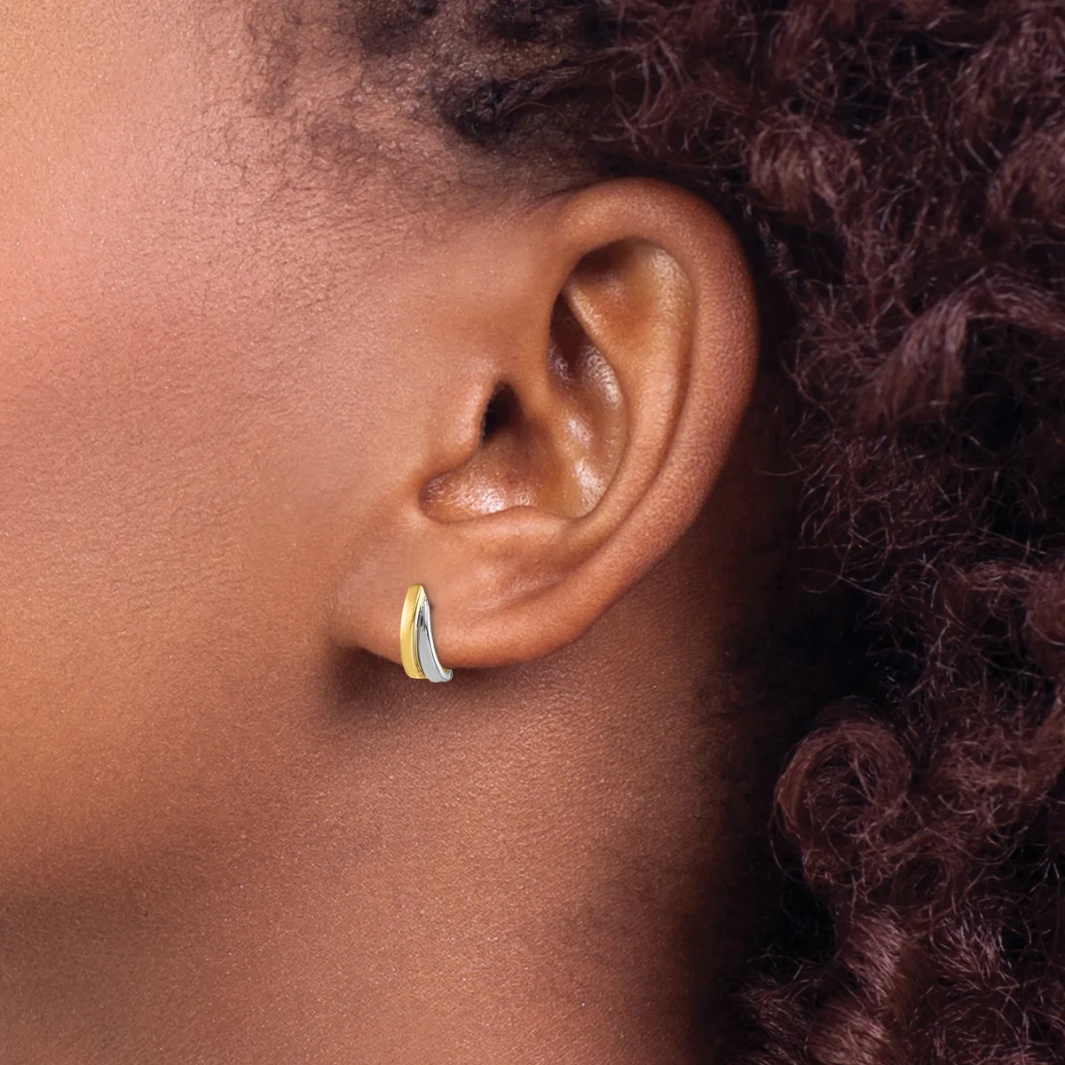 A person wearing a curved silver hoop earring in their earlobe, shown in profile with textured dark hair visible in the background.