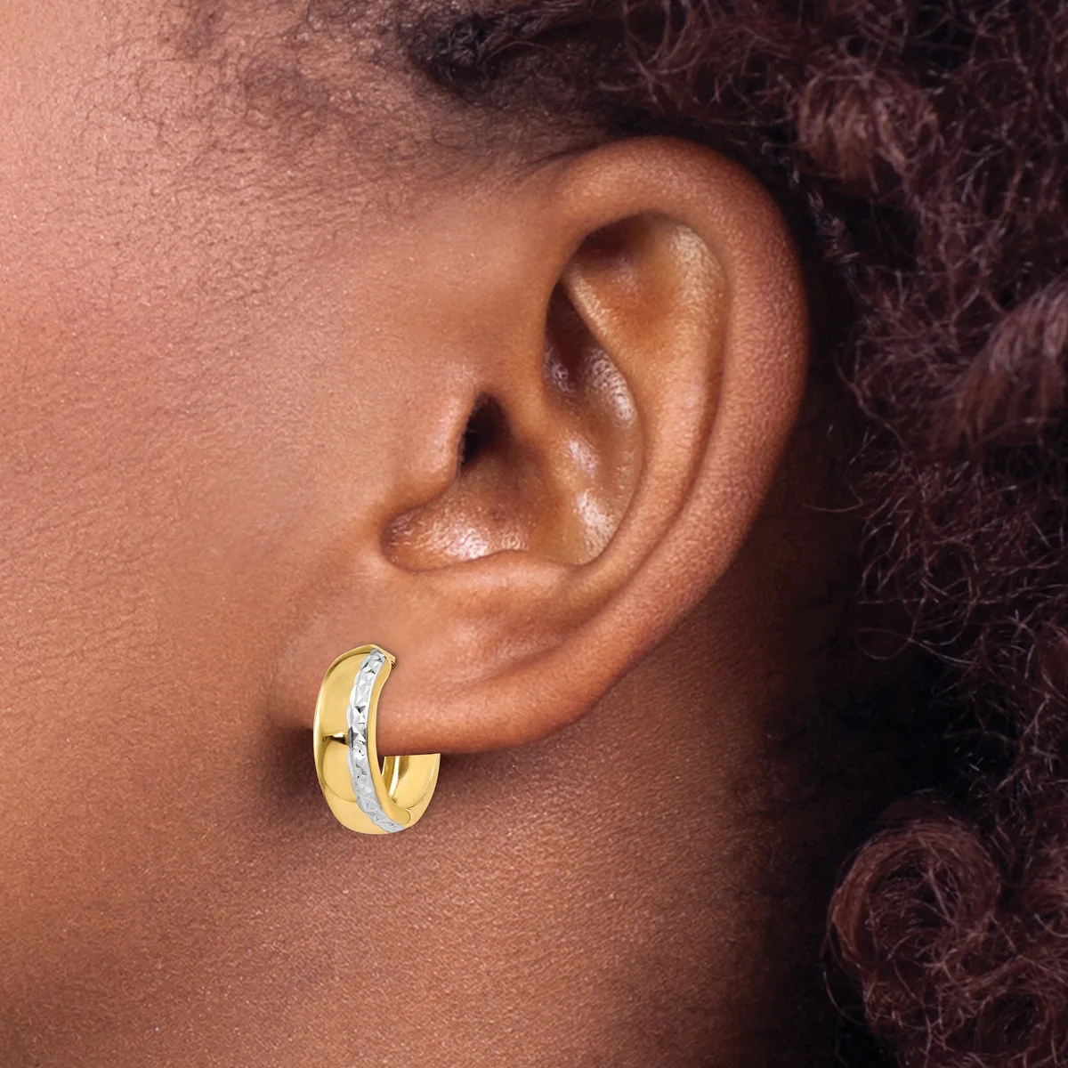 A gold and silver two-tone hoop earring worn on the earlobe of a person with dark skin and textured hair.