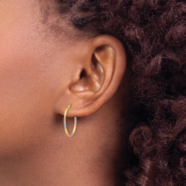 A person wearing a small gold hoop earring in their earlobe, shown in profile against their shoulder and dark curly hair.