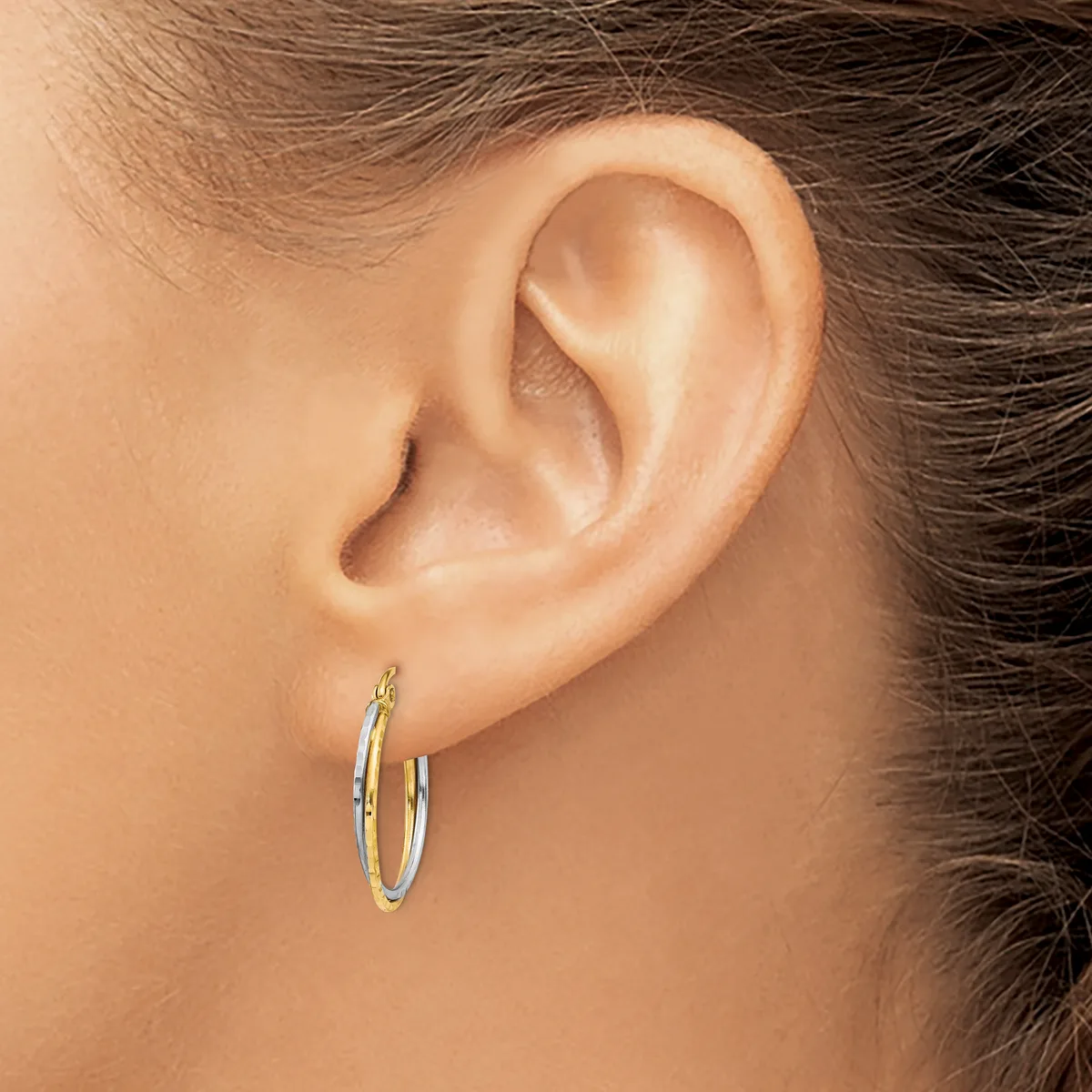 A person wearing two-tone gold hoop earrings with a textured finish, shown from the side view of their ear and head.