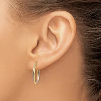A person wearing two-tone gold hoop earrings with a textured finish, shown from the side view of their ear and head.