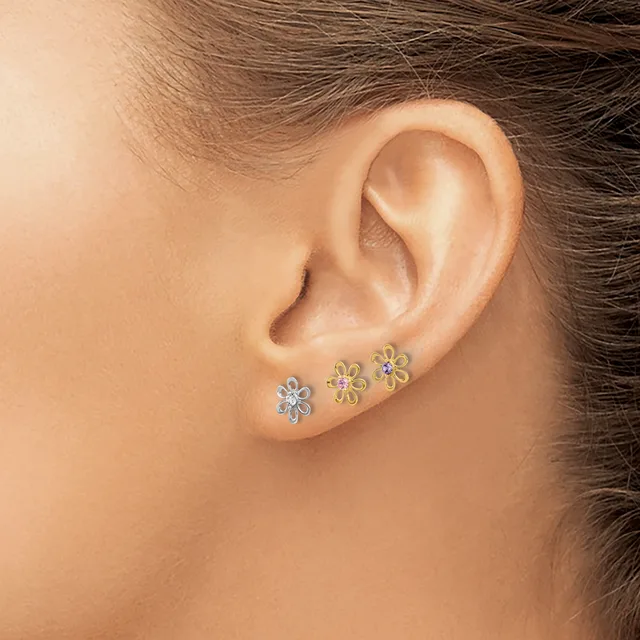 A person wearing three small flower-shaped stud earrings in silver and gold metals along the earlobe.