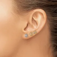 A person wearing three small flower-shaped stud earrings in silver and gold metals along the earlobe.