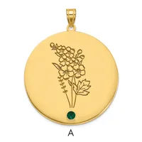 Gold circular pendant with engraved flower cluster design and a small green gemstone at the bottom, shown with gold bail loop.