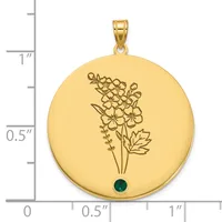 Gold-colored round pendant with engraved flowers and leaves, featuring a small dark green gemstone at the bottom, shown next to a ruler for scale.
