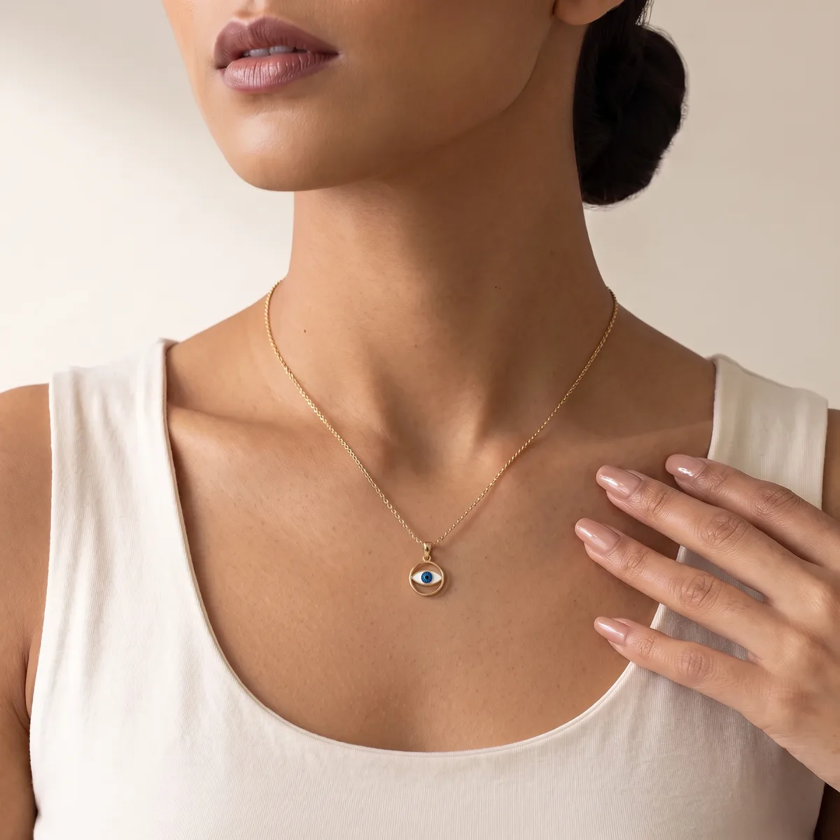 Woman wearing a white sleeveless top and a silver chain necklace with a small circular pendant featuring a dark blue stone.