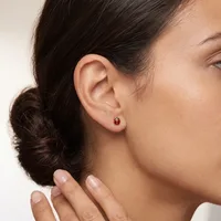 Woman wearing a small red gemstone stud earring in her earlobe, shown in profile against a neutral background.