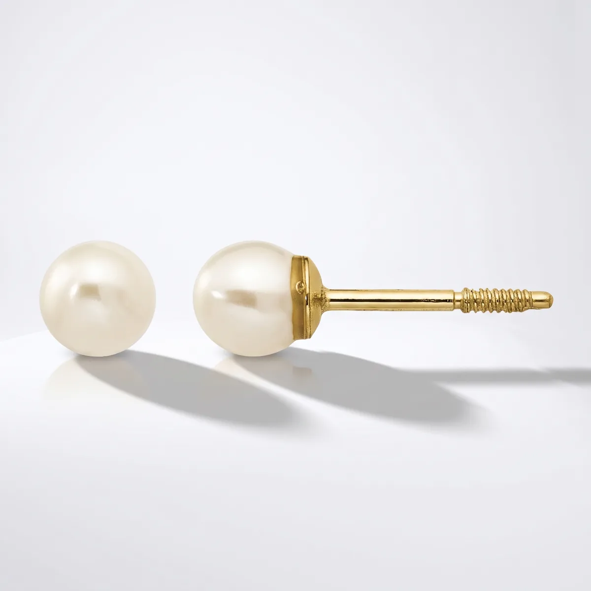 A pair of pearl stud earrings with cream-colored round pearls mounted on gold posts with threaded backs, shown from front and side angles.