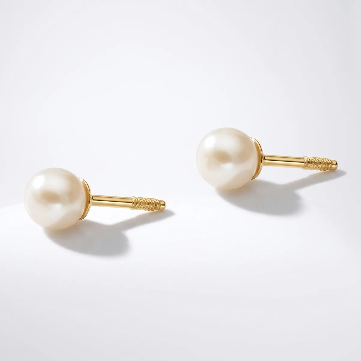 A pair of gold stud earrings with cream-colored pearl tops and threaded posts, displayed on a light gray background.