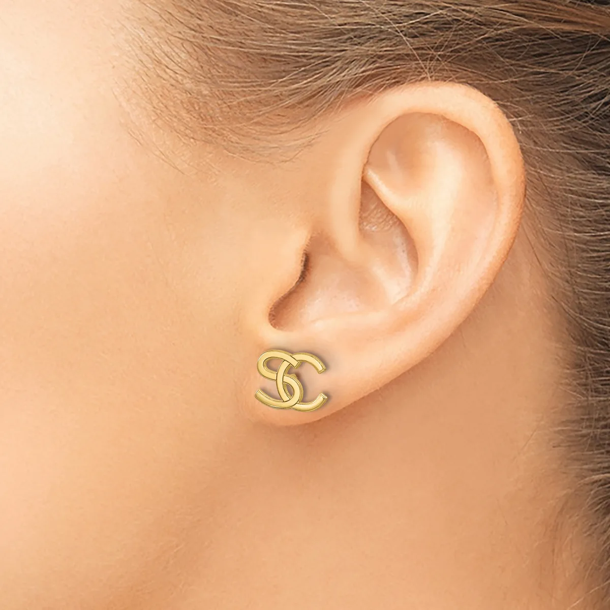 A gold-toned stud earring with an interlocking curved design worn on a person's earlobe.