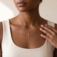 A person wearing a white sleeveless top and a gold chain necklace with a curved pendant.