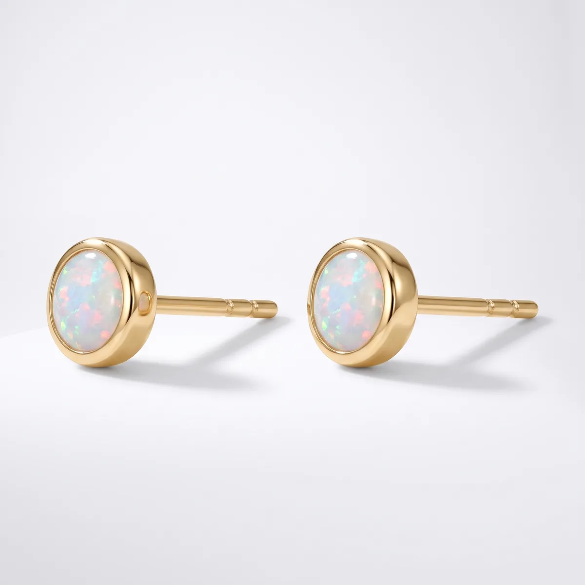 A pair of gold stud earrings with oval opals set in round bezels, shown from the front against a white background.