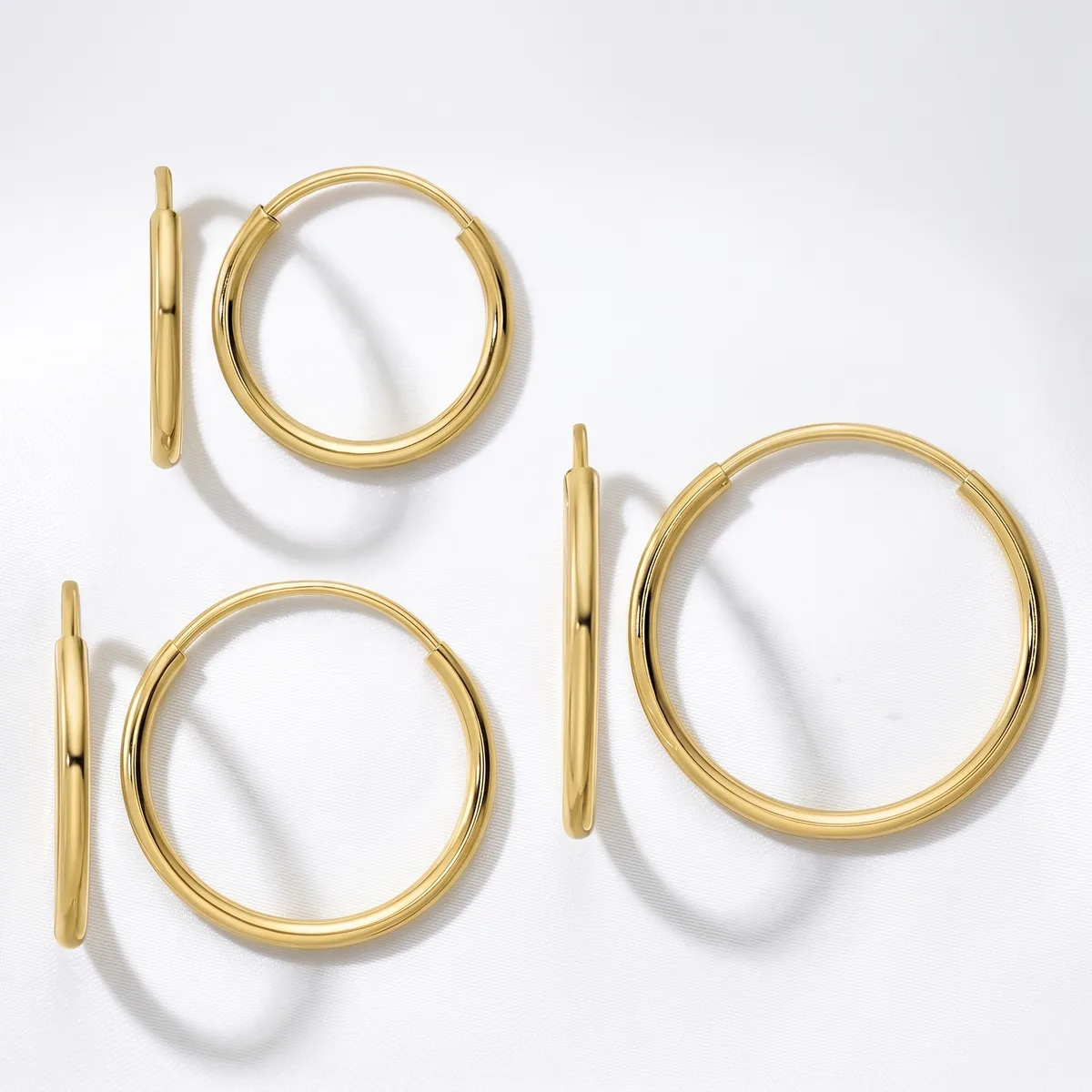 Three pairs of polished gold hoop earrings in varying sizes arranged on a white surface, each pair shown from the front and side view.