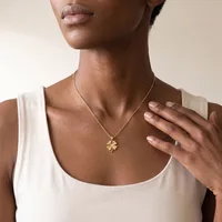 A person wearing a white sleeveless tank top and a gold four-leaf clover pendant necklace, shown from the neck down.