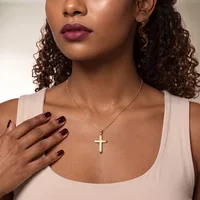 Woman wearing a white sleeveless top and a gold cross pendant necklace, with burgundy nail polish and mauve lipstick.