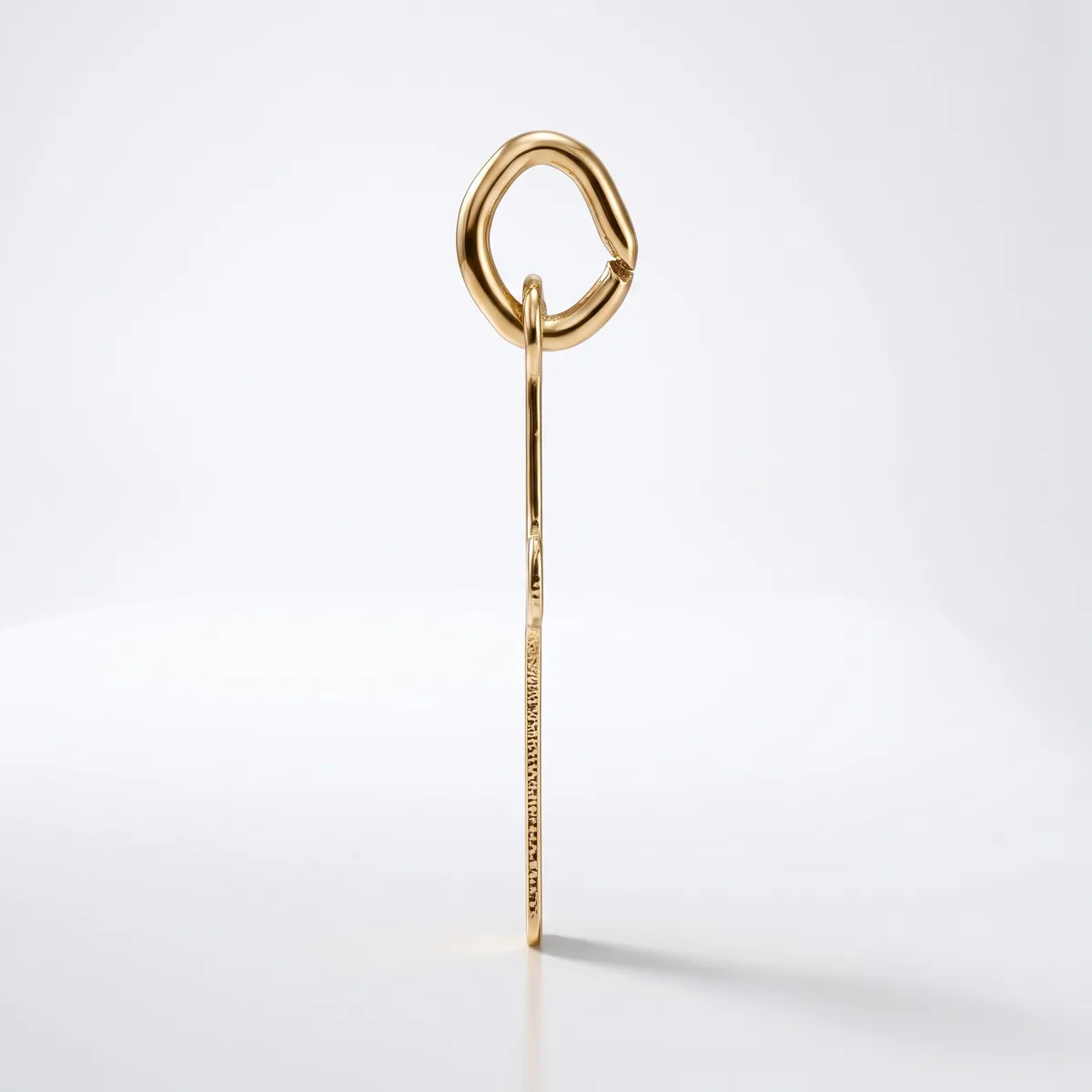 A gold-toned metal hair stick with a decorative loop handle at the top and fine textured detailing along the shaft, displayed vertically against a white background.