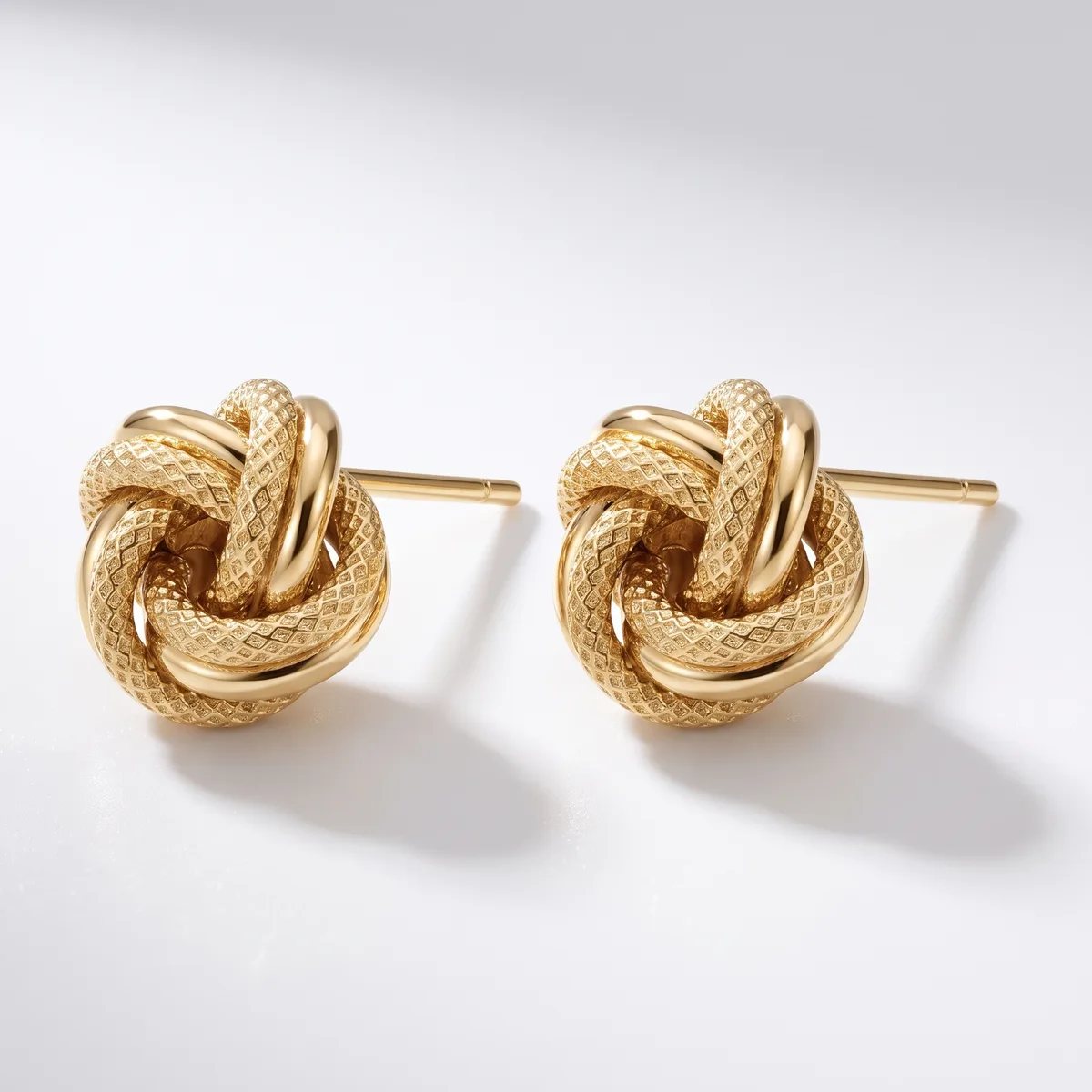 A pair of gold-toned knot stud earrings with a textured finish, displayed against a white background.