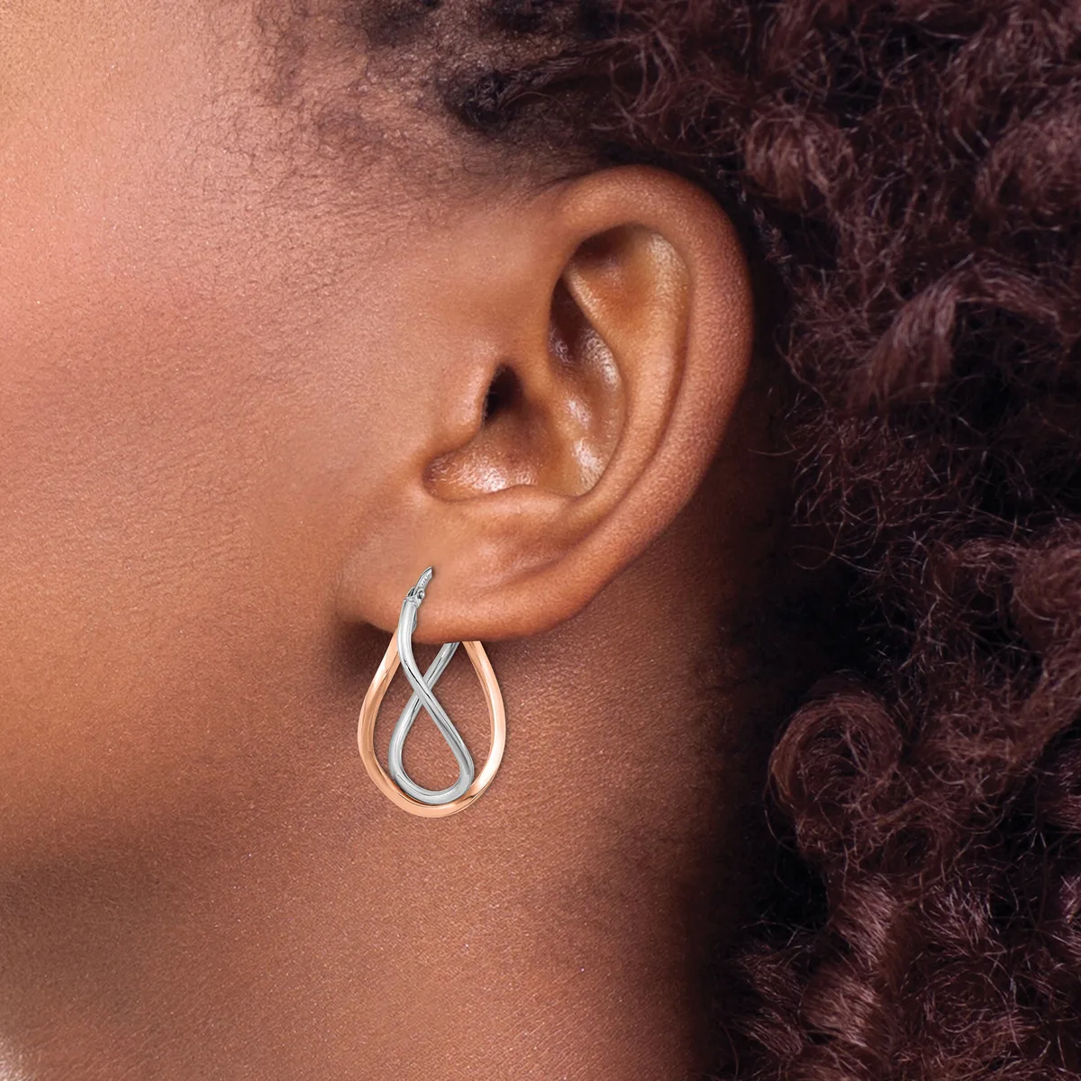 A person wearing a silver twisted teardrop hoop earring on their earlobe, shown from the side profile.