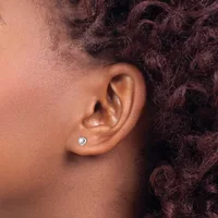 A person with dark curly hair wears a small round stud earring with a light blue stone in their earlobe.