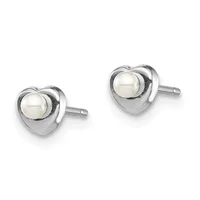 A pair of heart-shaped stud earrings in polished silver metal, each featuring a round white pearl set in the center, shown from the front against a white background.