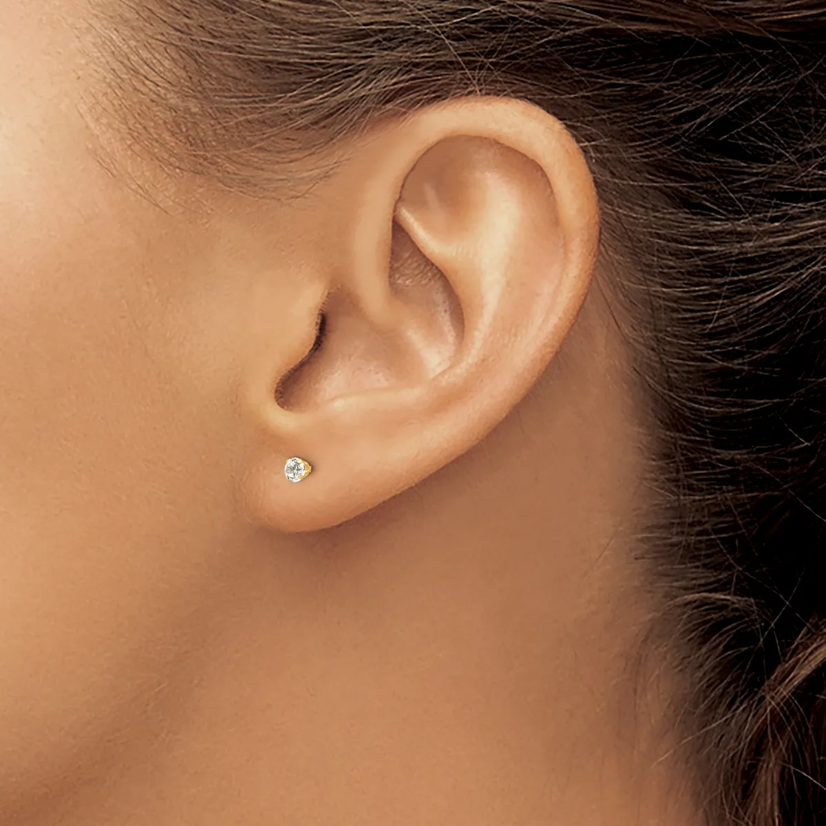A person's ear wearing a small round diamond stud earring in a white metal setting.