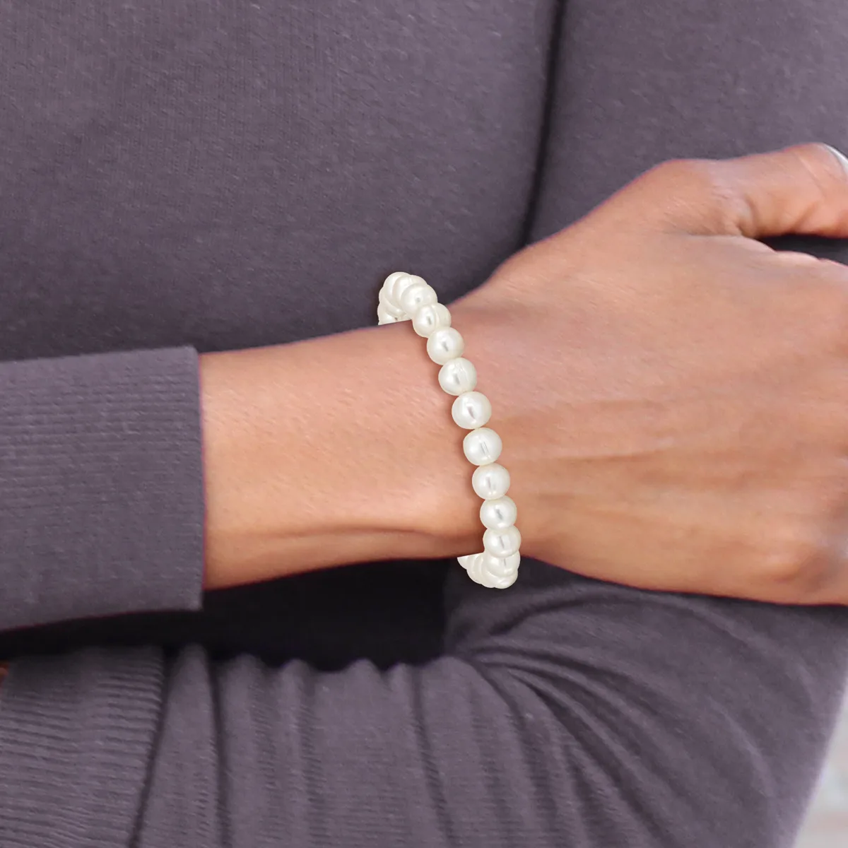 A person wearing a gray long-sleeved top displays a beaded bracelet made of white round pearls on their wrist.