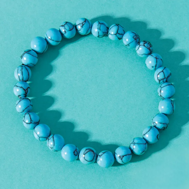 A circular bracelet made of light blue beads with dark veining or crackle pattern, arranged on a matching turquoise background.