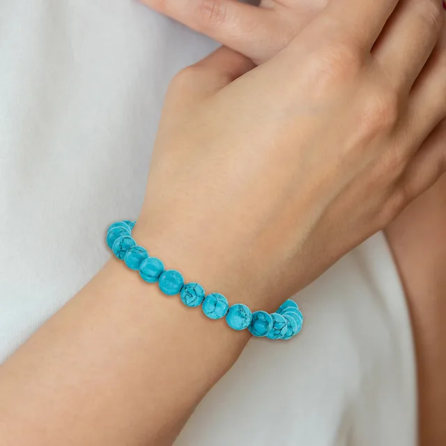 A person wearing a turquoise beaded bracelet with round crackle-finish stones strung together on an elastic band.
