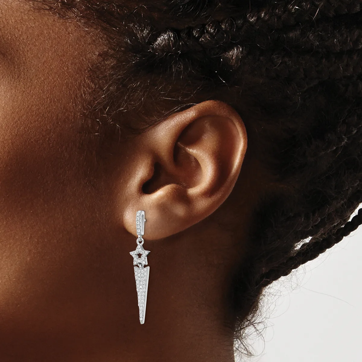A person wearing a long, pointed silver drop earring with a star-shaped top and pave-set stones, shown from the side profile against a neutral background.
