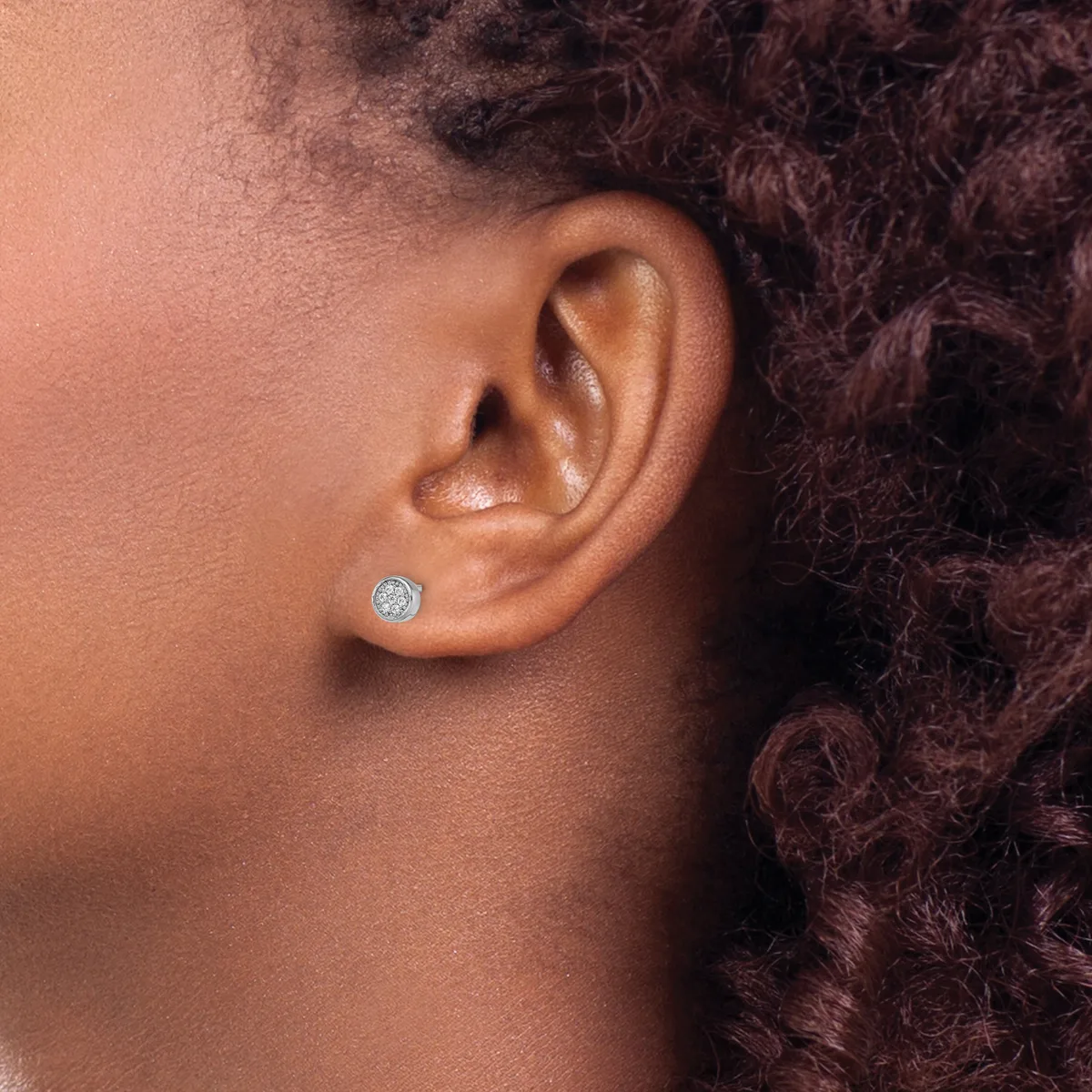 Close-up side view of a person's ear wearing a small round stud earring with a clear gemstone in a silver-toned setting.