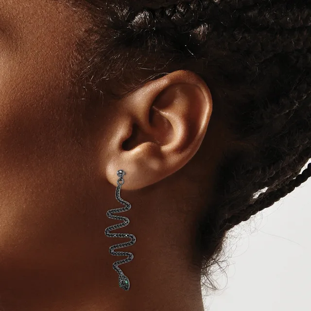 A person wearing a long, sinuous snake-shaped earring with blue gemstones, shown from the side view of their ear and neck.