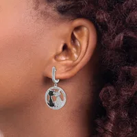 A silver hoop earring with a circular pendant featuring two cats and decorative details hangs from a person's earlobe.