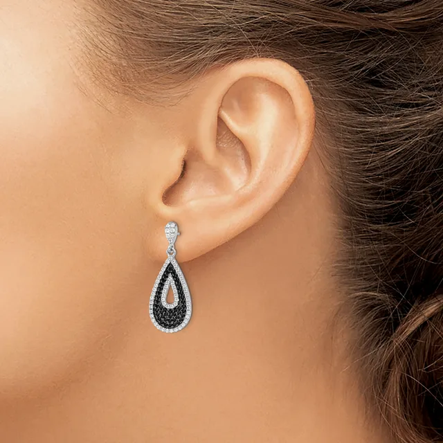A teardrop-shaped dangle earring with black and white diamonds in a twisted design, worn on a person's earlobe.