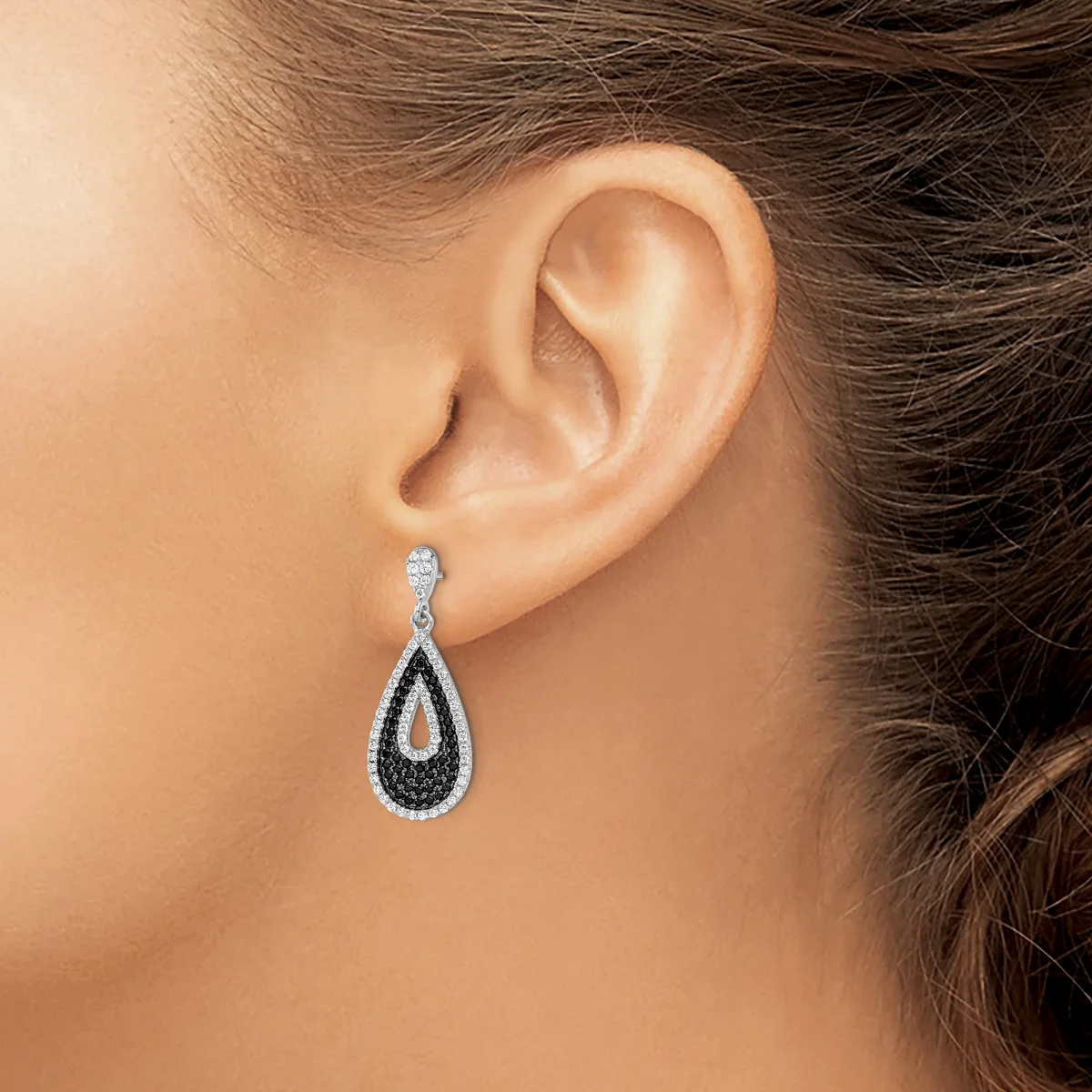 A teardrop-shaped dangle earring with black and white diamonds in a twisted design, worn on a person's earlobe.