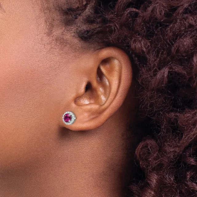 A close-up side view of a person's ear wearing a round stud earring with a red gemstone center surrounded by small white stones in a silver-toned metal setting.