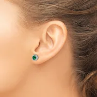 A person wearing a small round stud earring with a green stone surrounded by a silver-toned metal halo setting in their pierced earlobe.