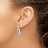 A person wearing a silver drop earring with interlocking oval loops and textured surface detail, shown from the side view of their ear.