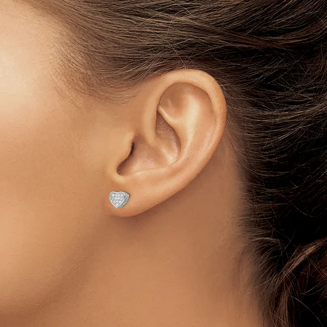A person wearing a small heart-shaped stud earring with a pave diamond setting in white metal, shown on their earlobe.