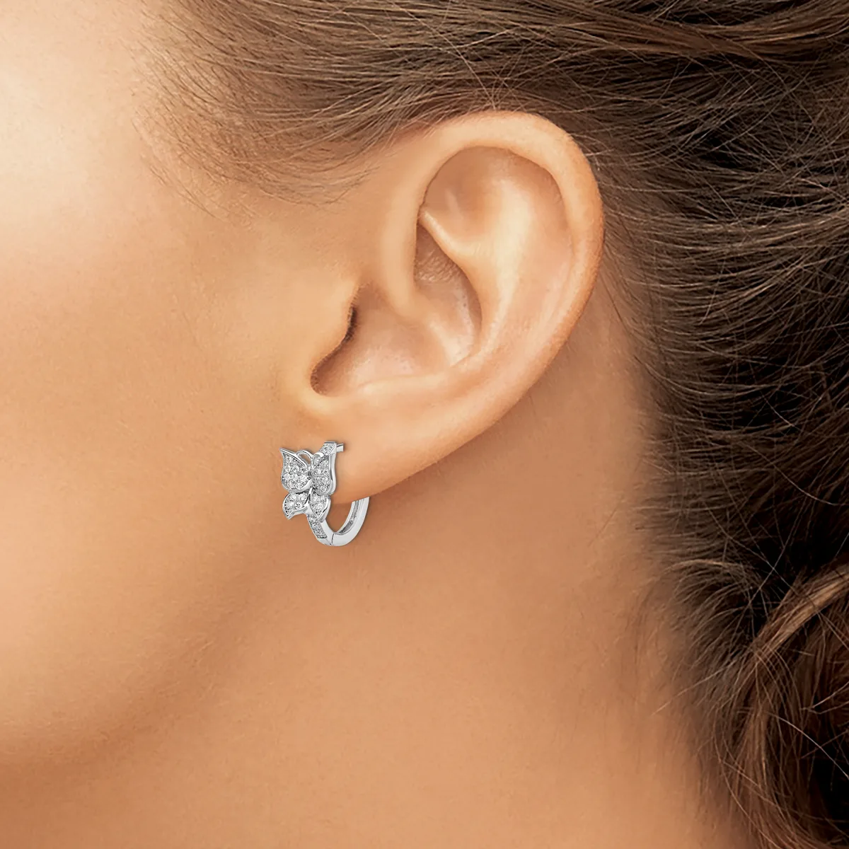 A woman wearing a small silver hoop earring with a rectangular diamond or crystal stone accent, shown from the side view of her ear.