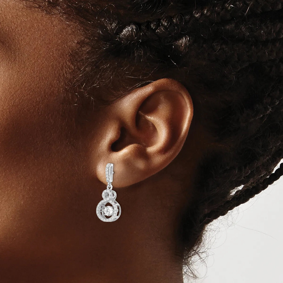 Close-up side view of a person's ear wearing a dangling silver earring with a rectangular top bar and a circular pendant adorned with a large round stone surrounded by smaller stones.