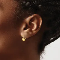 A close-up view of a person's ear wearing a small gold-colored hoop earring with a decorative charm hanging from it.