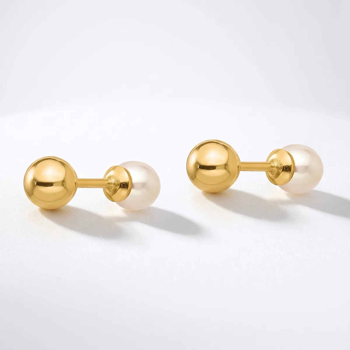 A pair of gold cufflinks with polished gold spheres connected to cream-colored pearl spheres, displayed on a white surface.